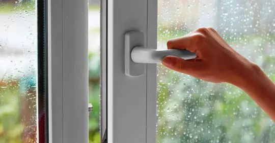 A female hand opens a window with water drops